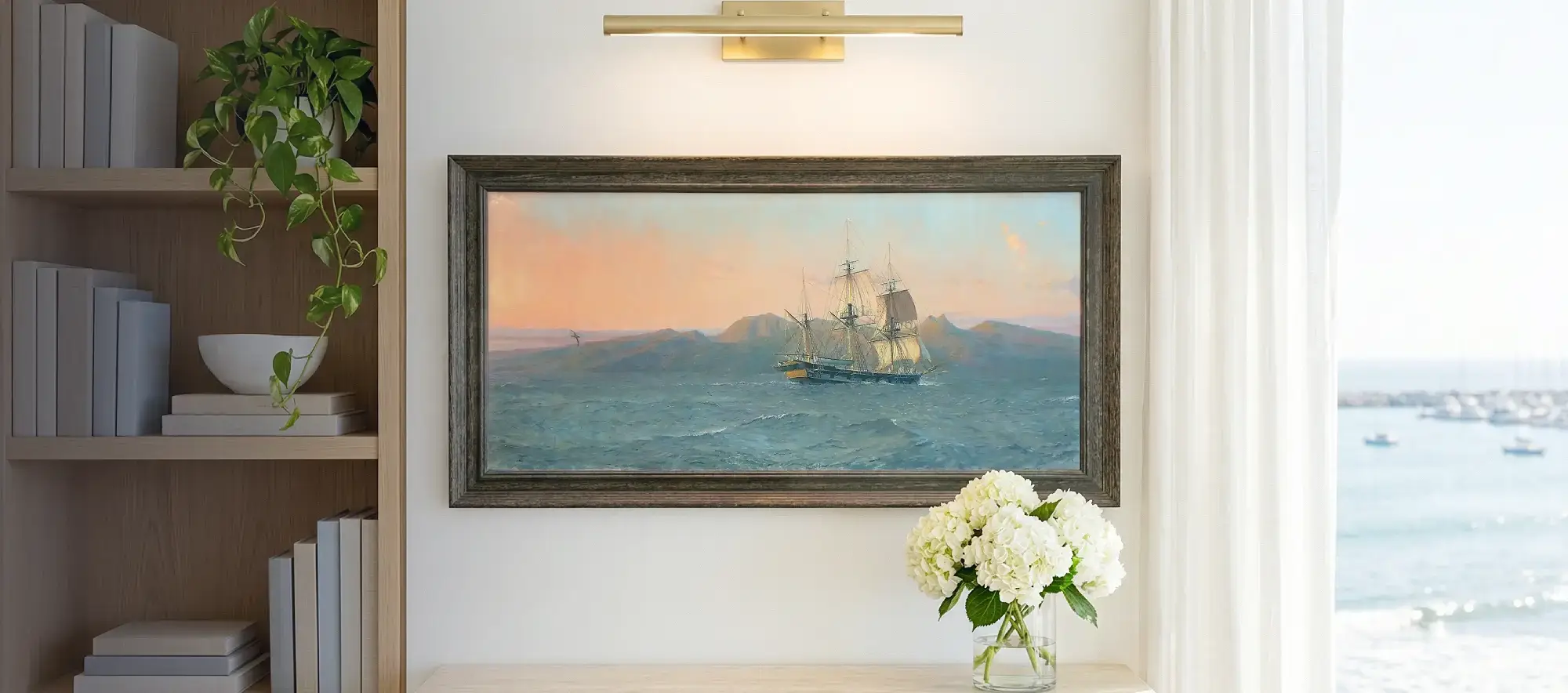 Framed panoramic painting of the Beagle hanging on a white wall above a light wood table with white hydrangeas, flanked by a modern bookcase.