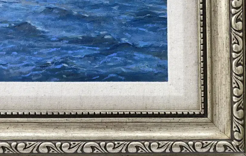 Close up of the ornate silver-toned picture frame and white linen slip, contrasting with the painted blue ocean waves.