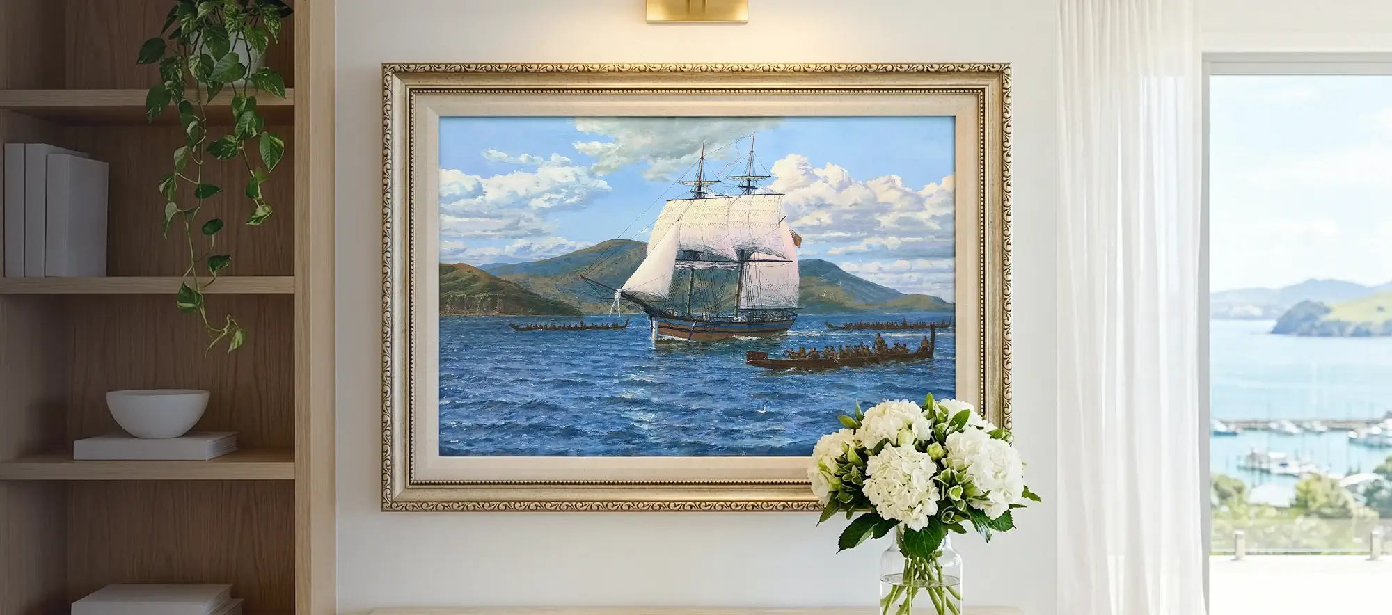 Framed painting of the Lady Nelson hanging on a white wall in a bright room with a bookcase and a coastal window view.