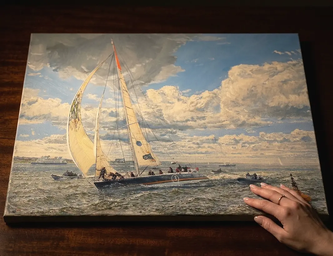 The unframed painted canvas held flat against a dark wooden table.