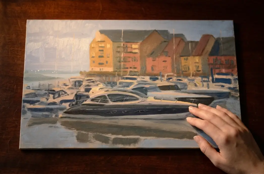 The unframed painted panel held flat against a dark wooden table by a hand.