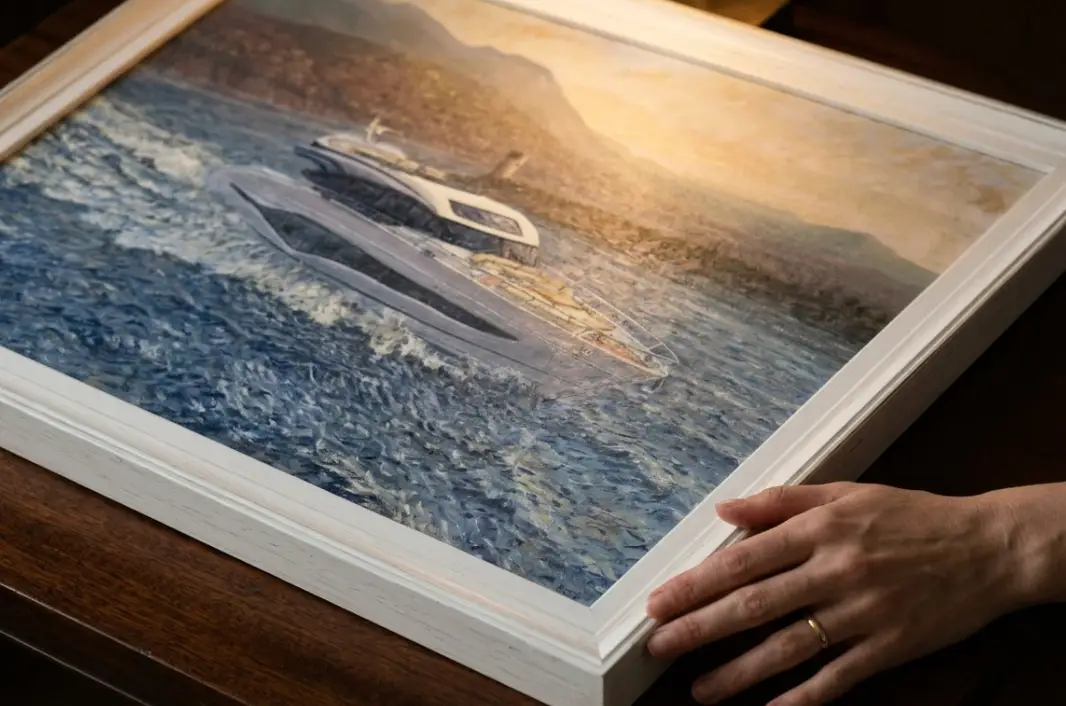 A person's hands adjusting the framed painting on a dark wooden surface.