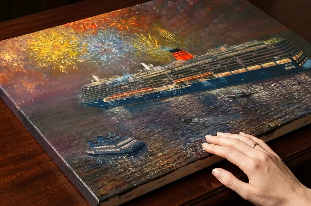 A person's hands resting near the edge of the unframed canvas, highlighting the painting's texture and colourful fireworks on a dark wooden table.
