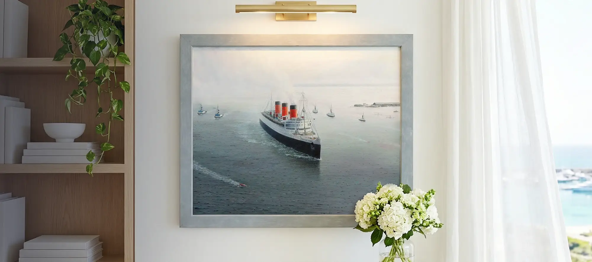 Framed painting of the Queen Mary hanging on a white wall above a light wood console table decorated with white hydrangeas.