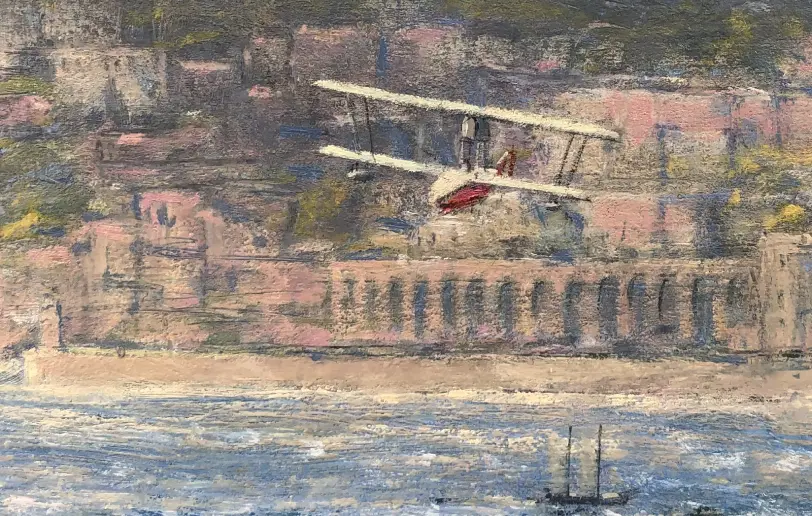 Close up of the background showing a distant competitor aircraft flying low past the historic archways and architecture of the Monaco coastline.