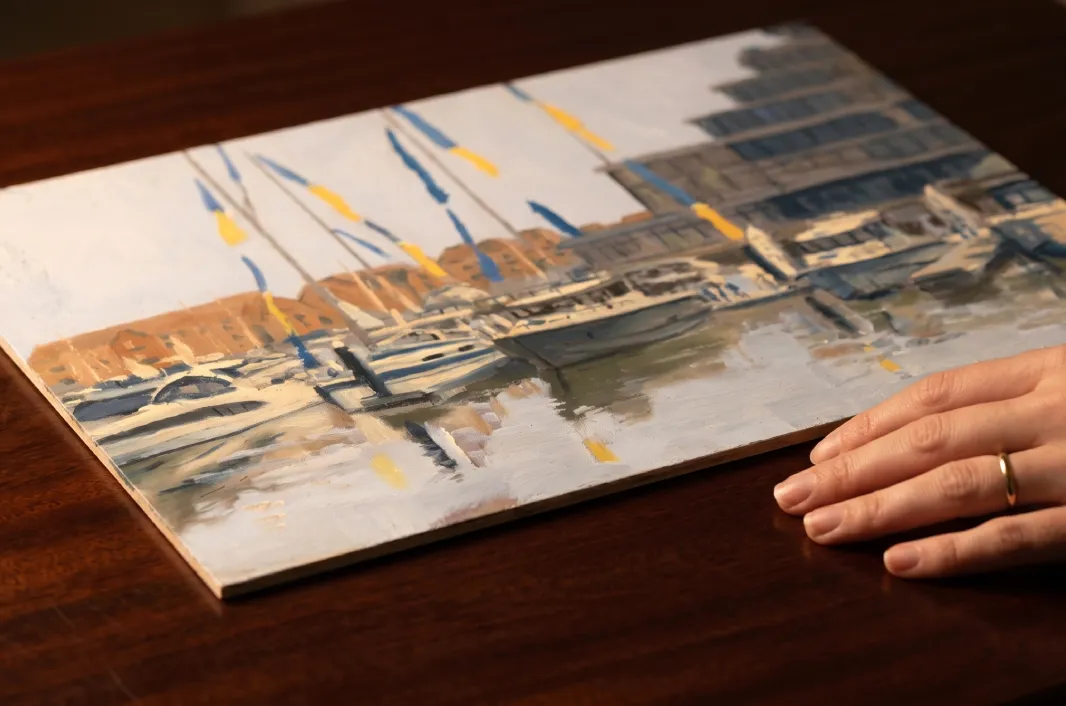 The oil painting resting on a dark wood table with a person's hand nearby for scale.