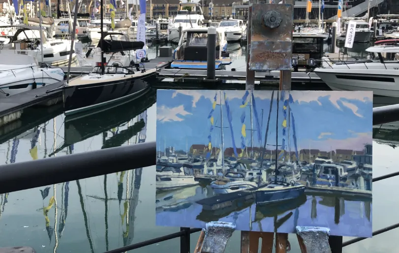 Close-up showing the painting on an easel in front of the actual marina view.