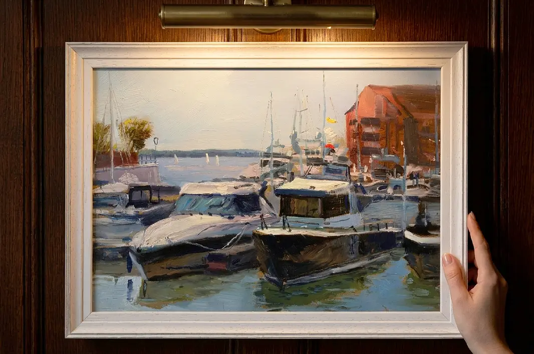 A person's hands adjusting the framed painting against rich dark wooden wall panelling under a warm picture light.