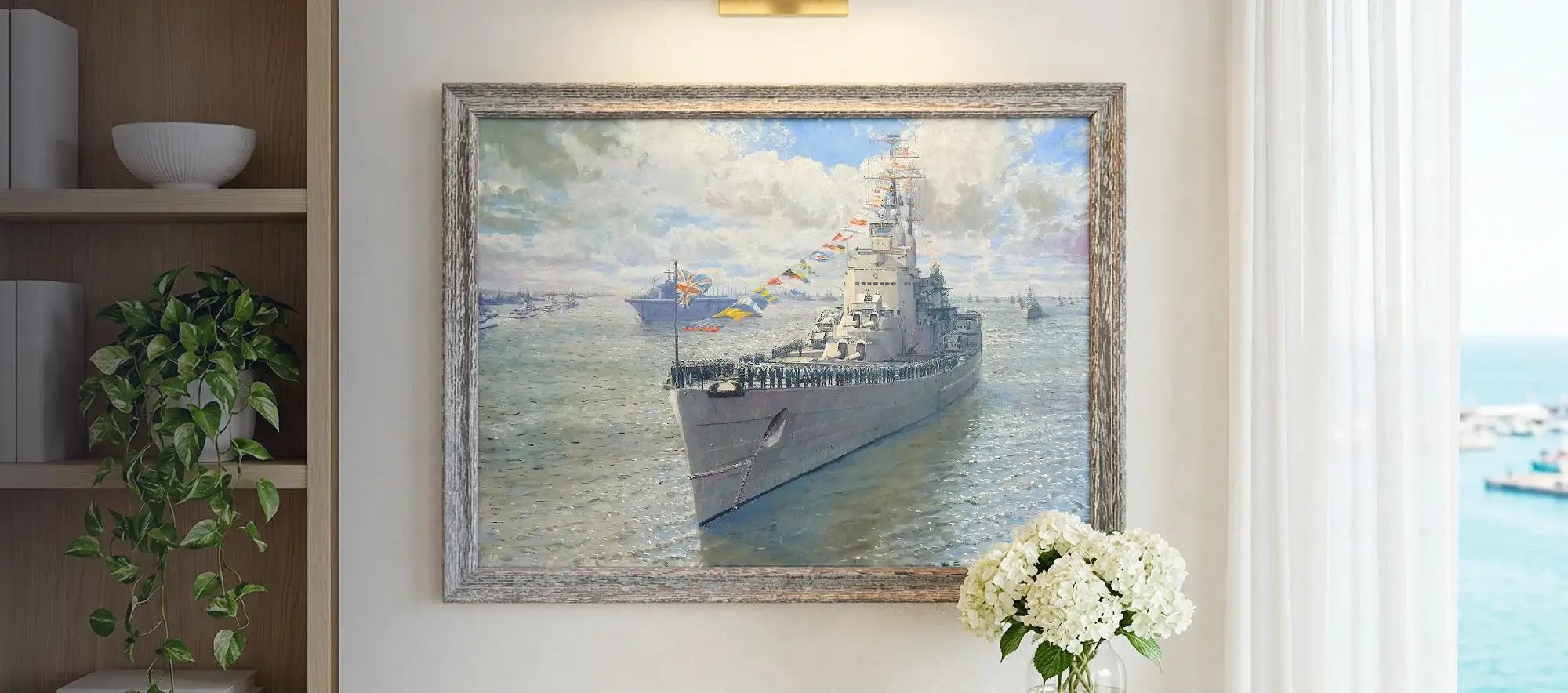 Framed painting of HMS Vanguard hanging on a white wall above a light wood table with white hydrangeas, flanked by a modern bookcase.